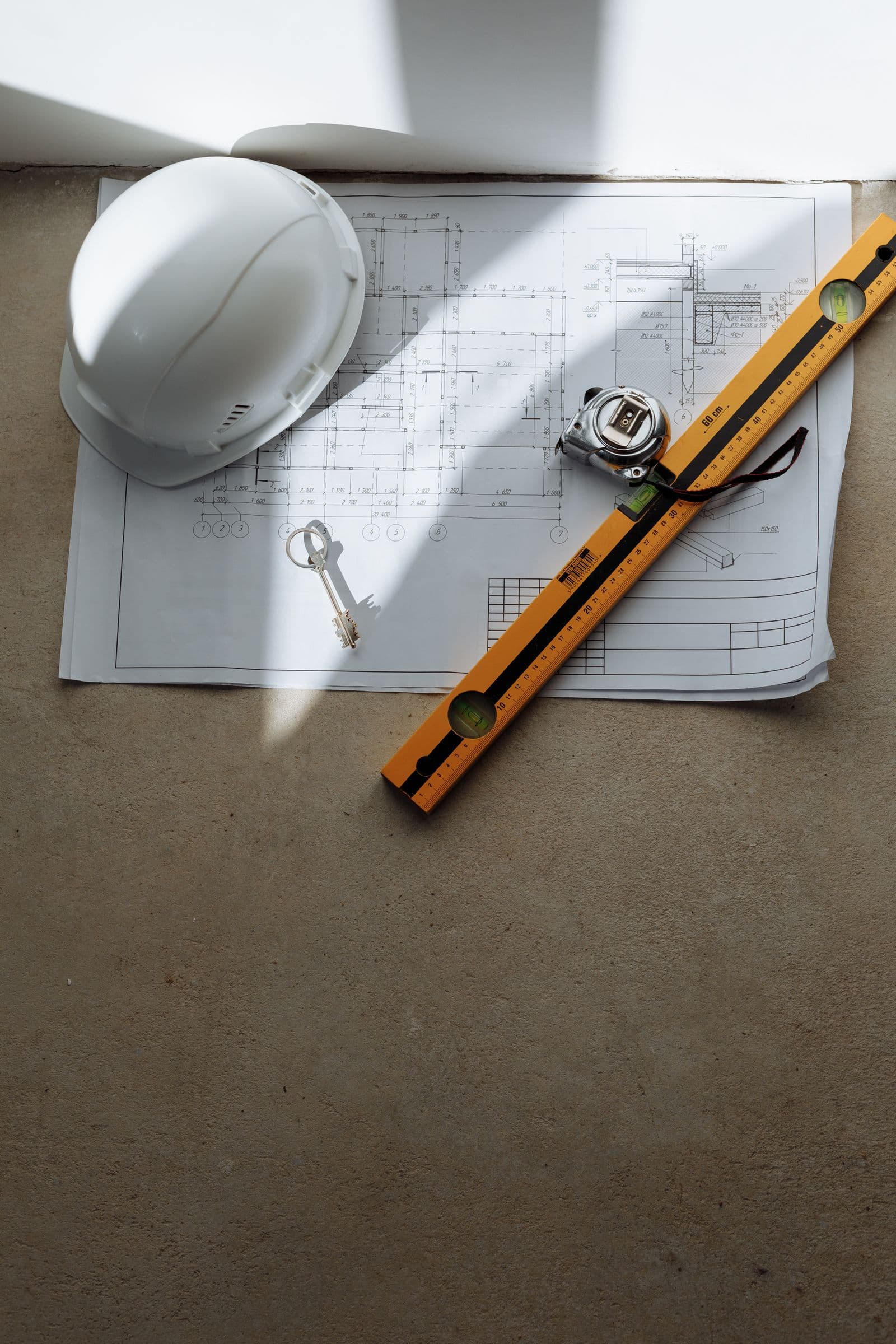 Hard hat, level and tape measure on a construction plan for flat-rate handyman pricing in Los Angeles