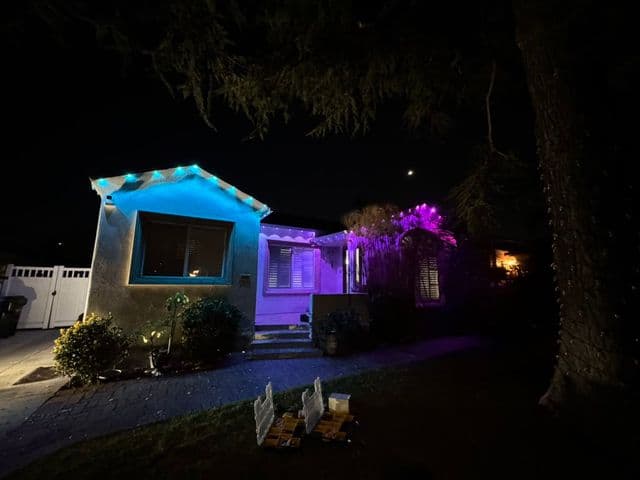 House lit in teal and purple at night with lights along the front walk. Work by Construction Hub in Los Angeles.