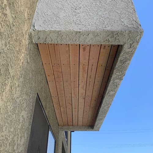 Finished wood plank soffit under stucco eave against blue sky. Work by Construction Hub in Los Angeles.