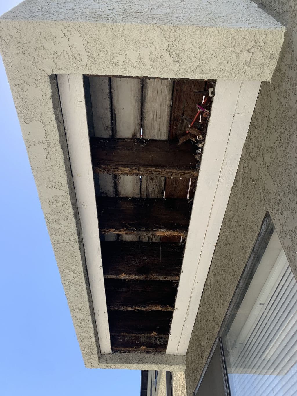 Damaged soffit removed showing weathered rafters under stucco eave. Work by Construction Hub in Los Angeles.