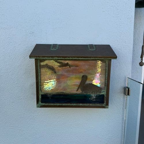 Patinated metal mailbox mounted on white stucco exterior wall. Work by Construction Hub in Los Angeles.