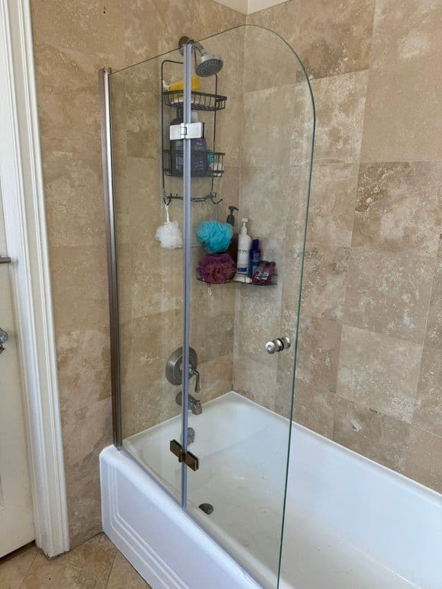 Glass shower screen installed on tub with travertine tile walls. Work by Construction Hub in Los Angeles.