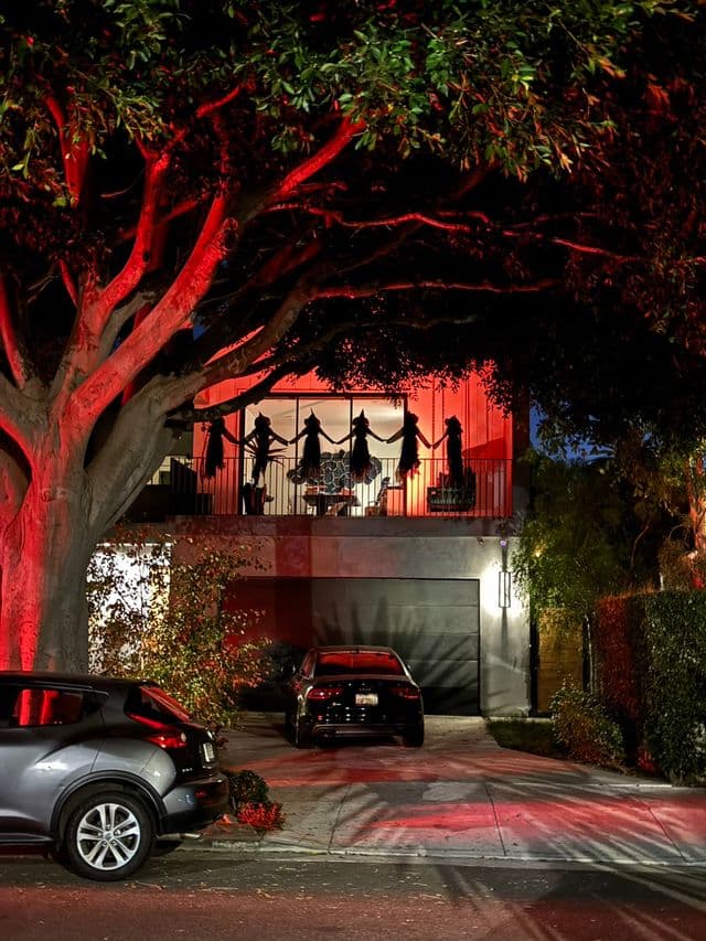 Halloween witch figures on balcony lit with red floodlights. Work by Construction Hub in Los Angeles.