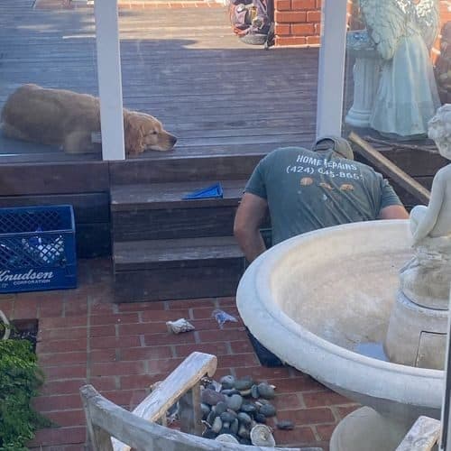 Worker repairing wood deck steps next to brick patio. Work by Construction Hub in Los Angeles.