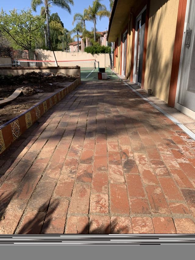 Long brick walkway running between a planter bed and a stucco building. Work by Construction Hub in Los Angeles.