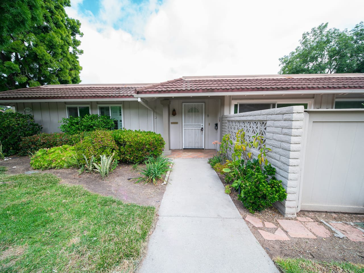 A single-story ranch house with a front walk, shrubs and a side gate
