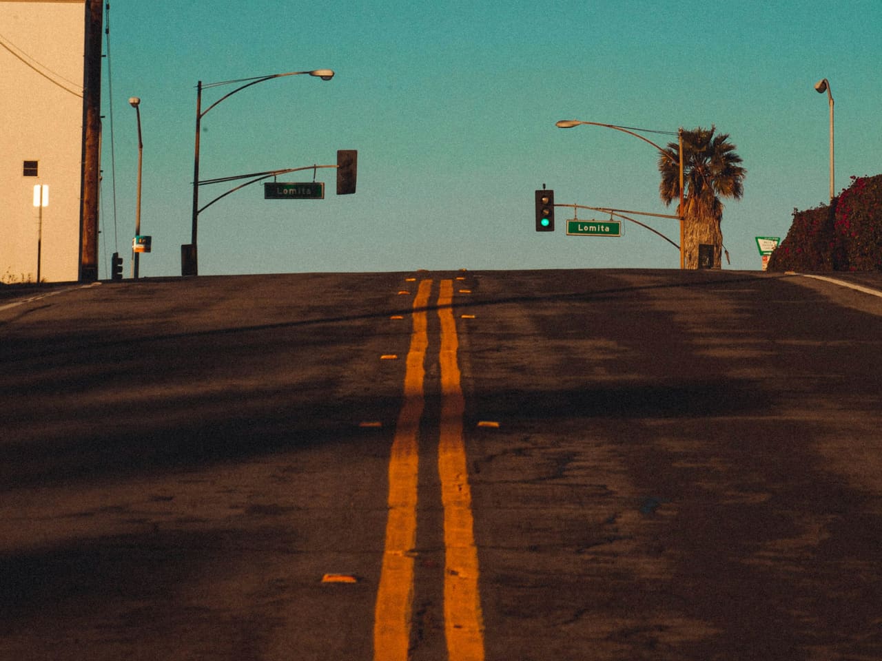 An empty El Segundo street at dawn with traffic lights, a Lomita Street sign and a palm tree