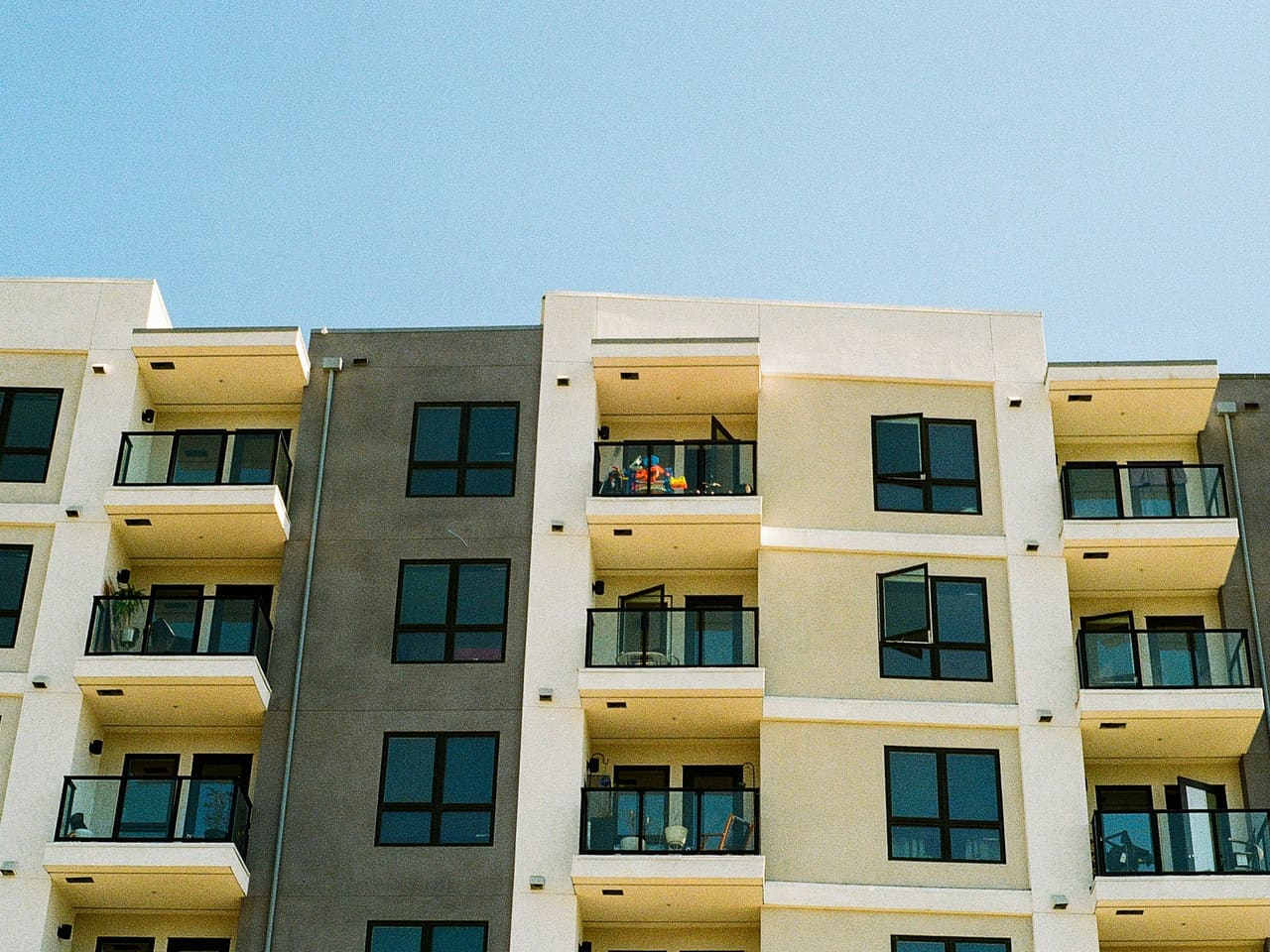 A cream and gray apartment building with glass balconies against a clear sky