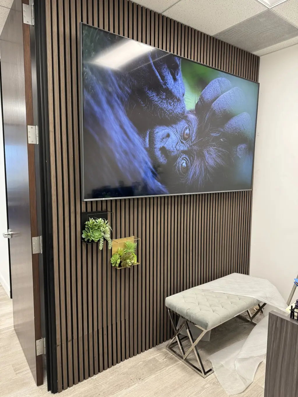 Large screen mounted on a wood slat wall beside a bench and small planters. Work by Construction Hub in Los Angeles.