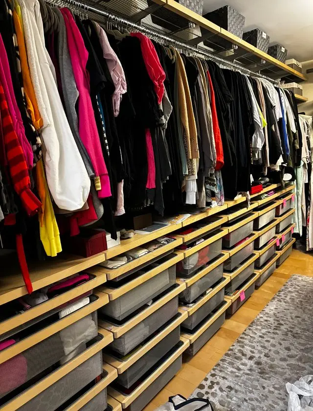 Finished walk-in closet filled with clothing and pull-out baskets. Work by Construction Hub in Los Angeles.
