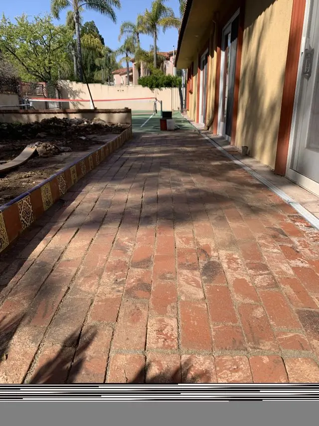 Long brick walkway running between a planter bed and a stucco building. Work by Construction Hub in Los Angeles.