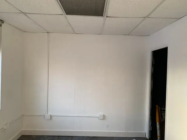 Office room painted white with a suspended ceiling and bare panelled walls. Work by Construction Hub in Los Angeles.