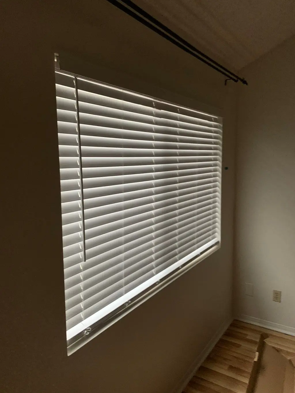 White faux wood blinds hung on a large window in empty room