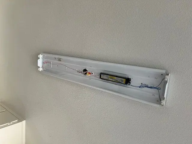 Fluorescent fixture opened on the wall showing the ballast and its wiring. Work by Construction Hub in Los Angeles.