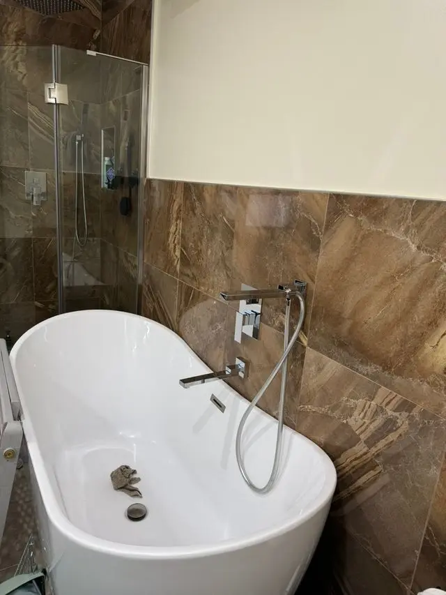 Chrome wall-mounted tub filler and handshower beside freestanding tub. Work by Construction Hub in Los Angeles.