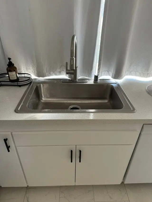 Stainless steel sink with pull-down faucet on white countertop. Work by Construction Hub in Los Angeles.