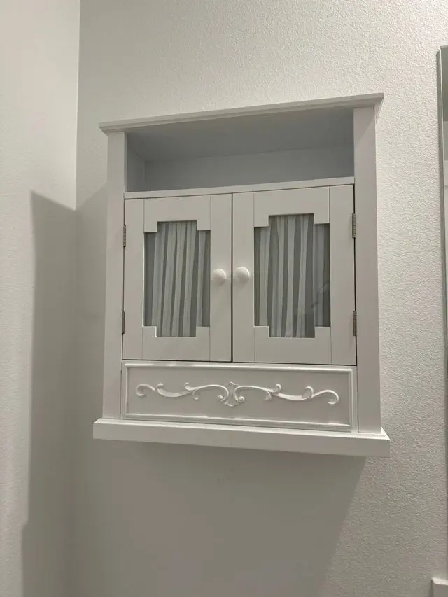 White wall cabinet with reeded glass doors and carved trim mounted on a plain wall. Work by Construction Hub in Los Angeles.