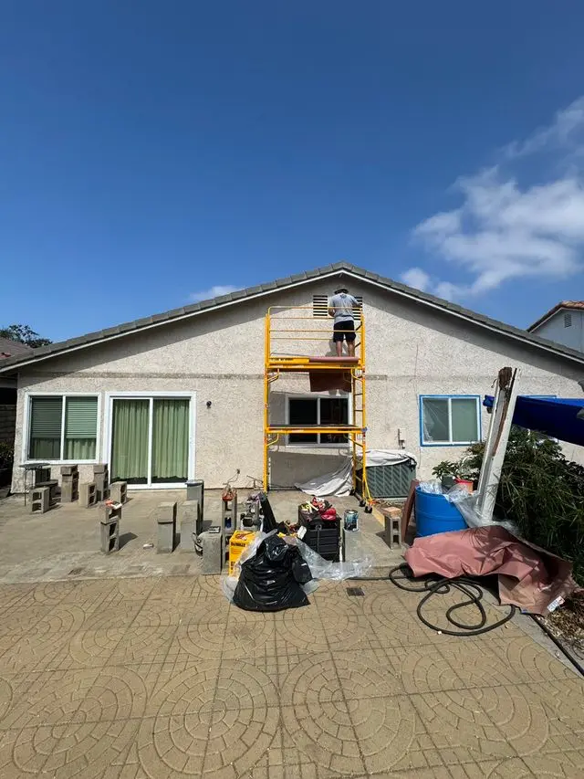 Scaffold against a stucco house with drop cloths and equipment across the driveway. Work by Construction Hub in Los Angeles.