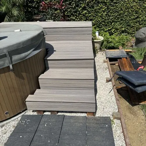 Composite deck stairs beside hot tub on gravel yard. Work by Construction Hub in Los Angeles.