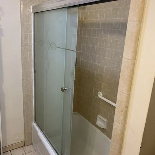 Sliding glass shower door open showing tiled tub surround and grab bar. Work by Construction Hub in Los Angeles.