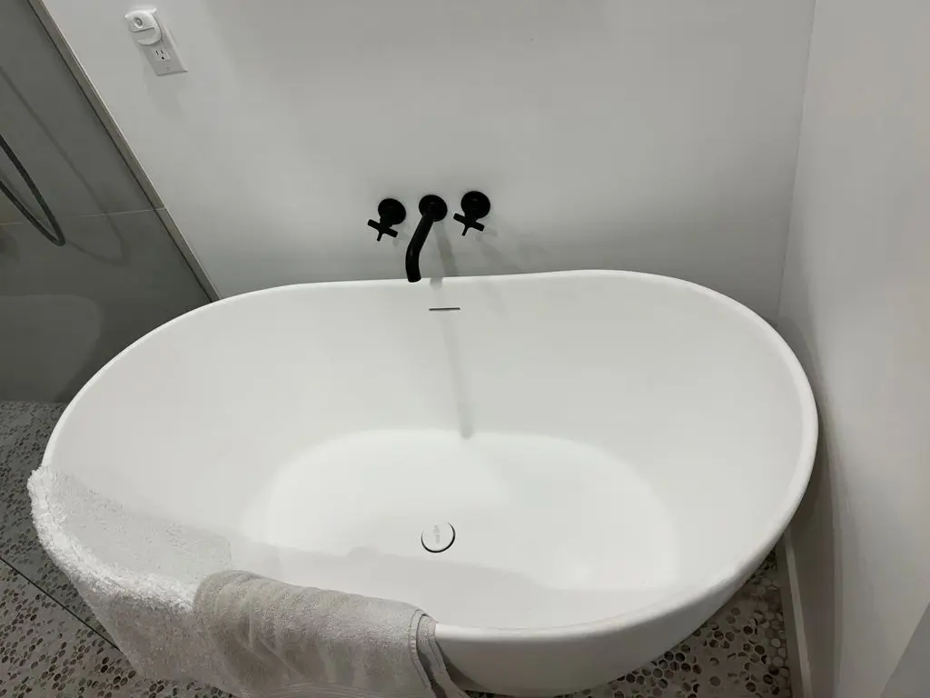 Wall-mounted black tub filler running into freestanding soaking tub. Work by Construction Hub in Los Angeles.