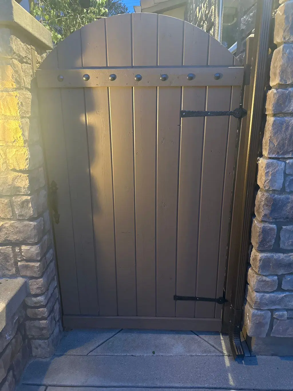 Arched wood gate painted brown between stone pillars. Work by Construction Hub in Los Angeles.