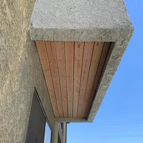 Finished wood plank soffit under stucco eave against blue sky. Work by Construction Hub in Los Angeles.