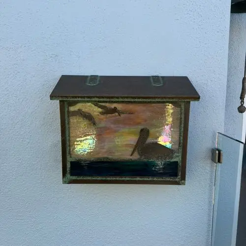 Patinated metal mailbox mounted on white stucco exterior wall. Work by Construction Hub in Los Angeles.