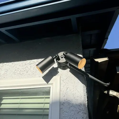 Black twin head floodlight installed under eave above window. Work by Construction Hub in Los Angeles.
