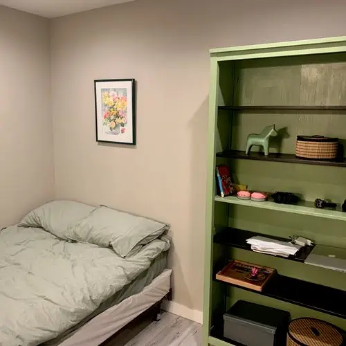Green painted built-in bookcase beside a bed and framed print. Work by Construction Hub in Los Angeles.