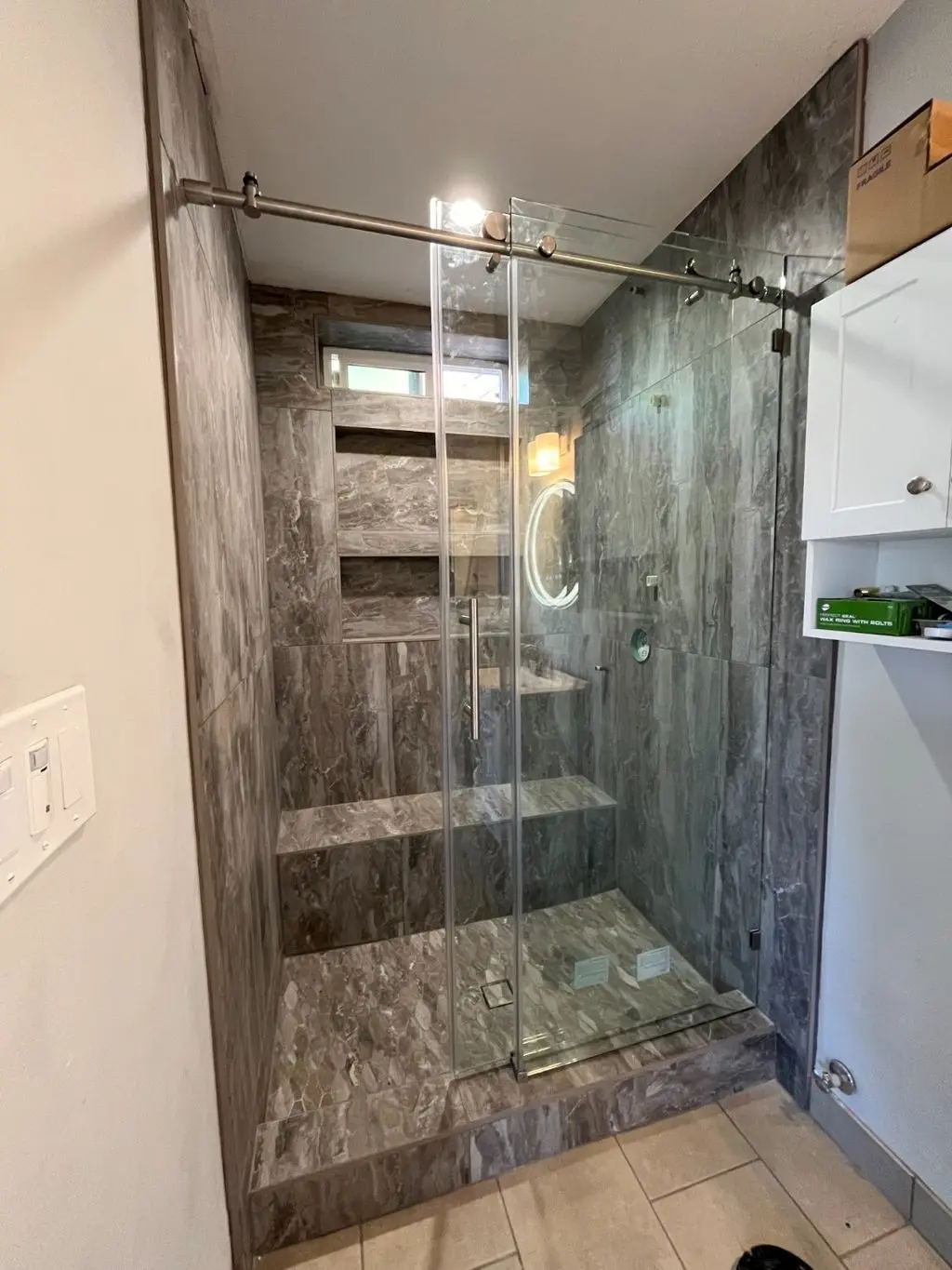 Tiled shower with glass sliding door, bench and built-in niches. Work by Construction Hub in Los Angeles.