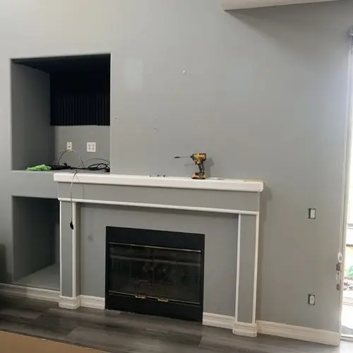 Bare grey wall above fireplace mantel with drill and open alcove. Work by Construction Hub in Los Angeles.