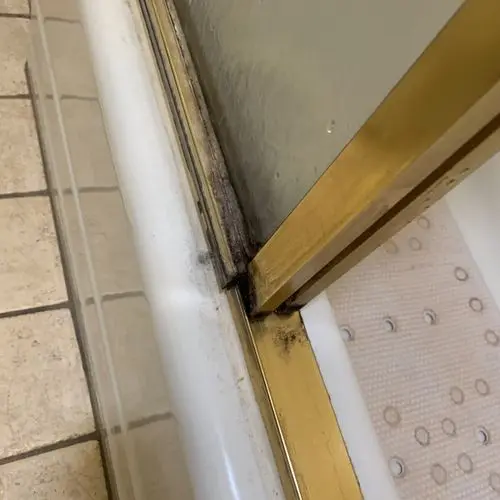 Old brass shower door track with blackened mold and failed caulk. Work by Construction Hub in Los Angeles.