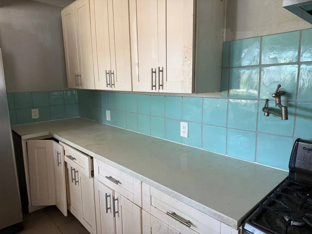 Teal square tile along a full kitchen counter, cut around the outlets, white shaker cabinets above. Work by Construction Hub in Los Angeles.