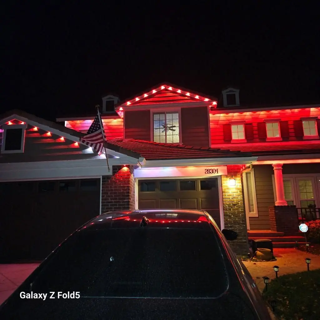 Two story house outlined in red lights at night with a flag above the garage. Work by Construction Hub in Los Angeles.