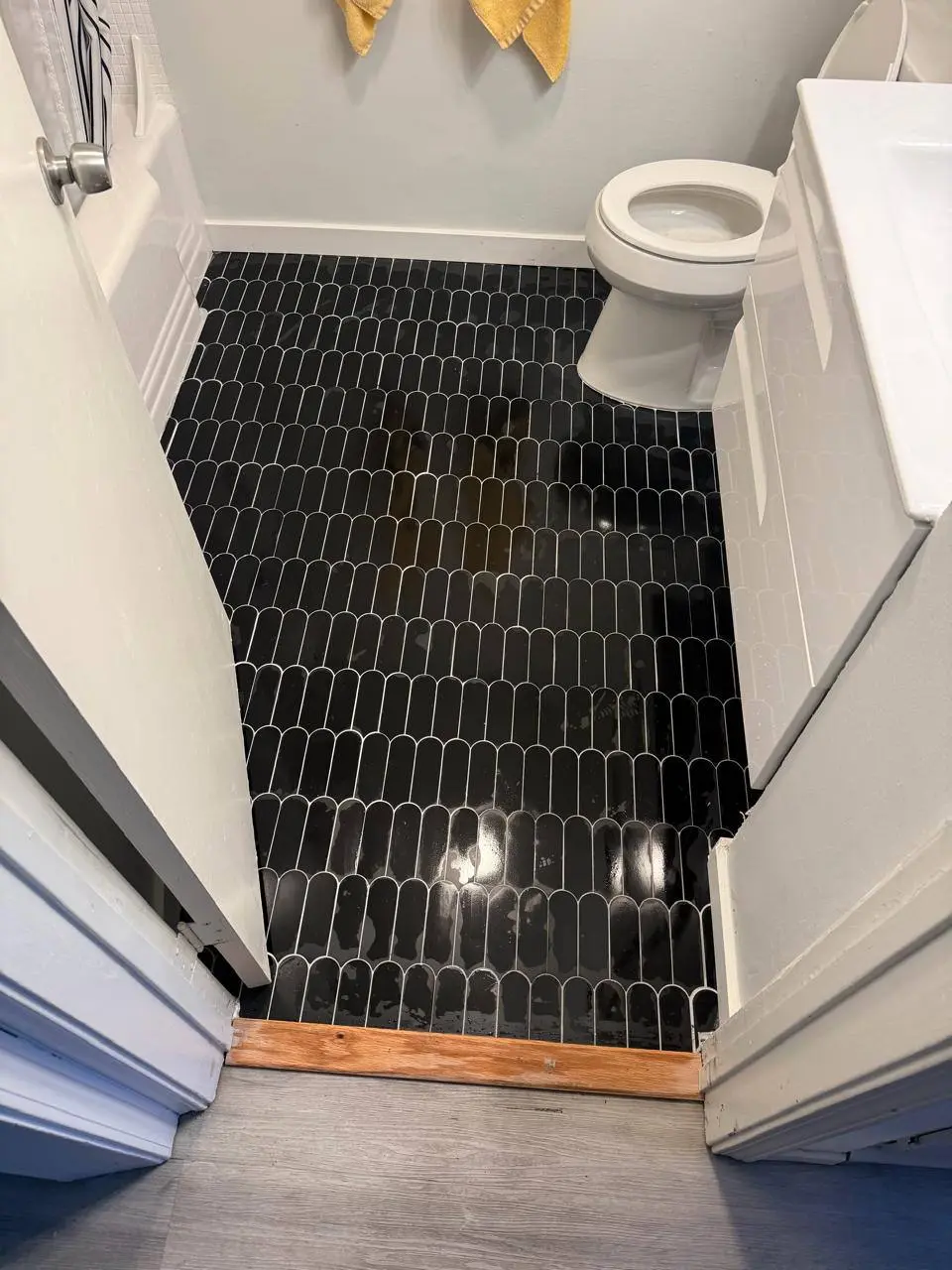 Dark elongated hex tile laid across a small bathroom floor around the toilet. Work by Construction Hub in Los Angeles.