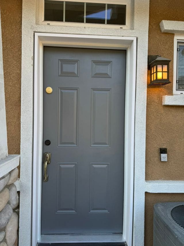 Grey six panel front door with a brass handle and a lantern beside it on stucco. Work by Construction Hub in Los Angeles.