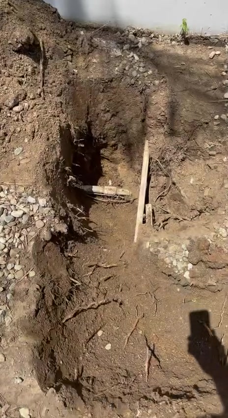 A piece of the old pipe at the bottom of a narrow hole, with roots tangled under it.