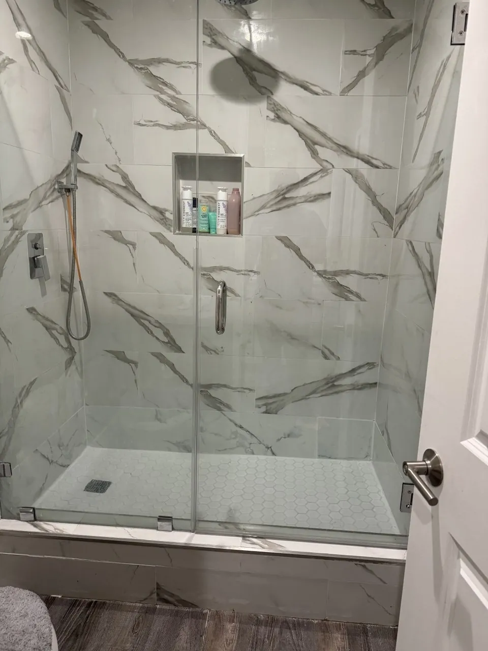 Finished walk-in shower with marble-look porcelain tile, niche, hand shower and frameless glass door