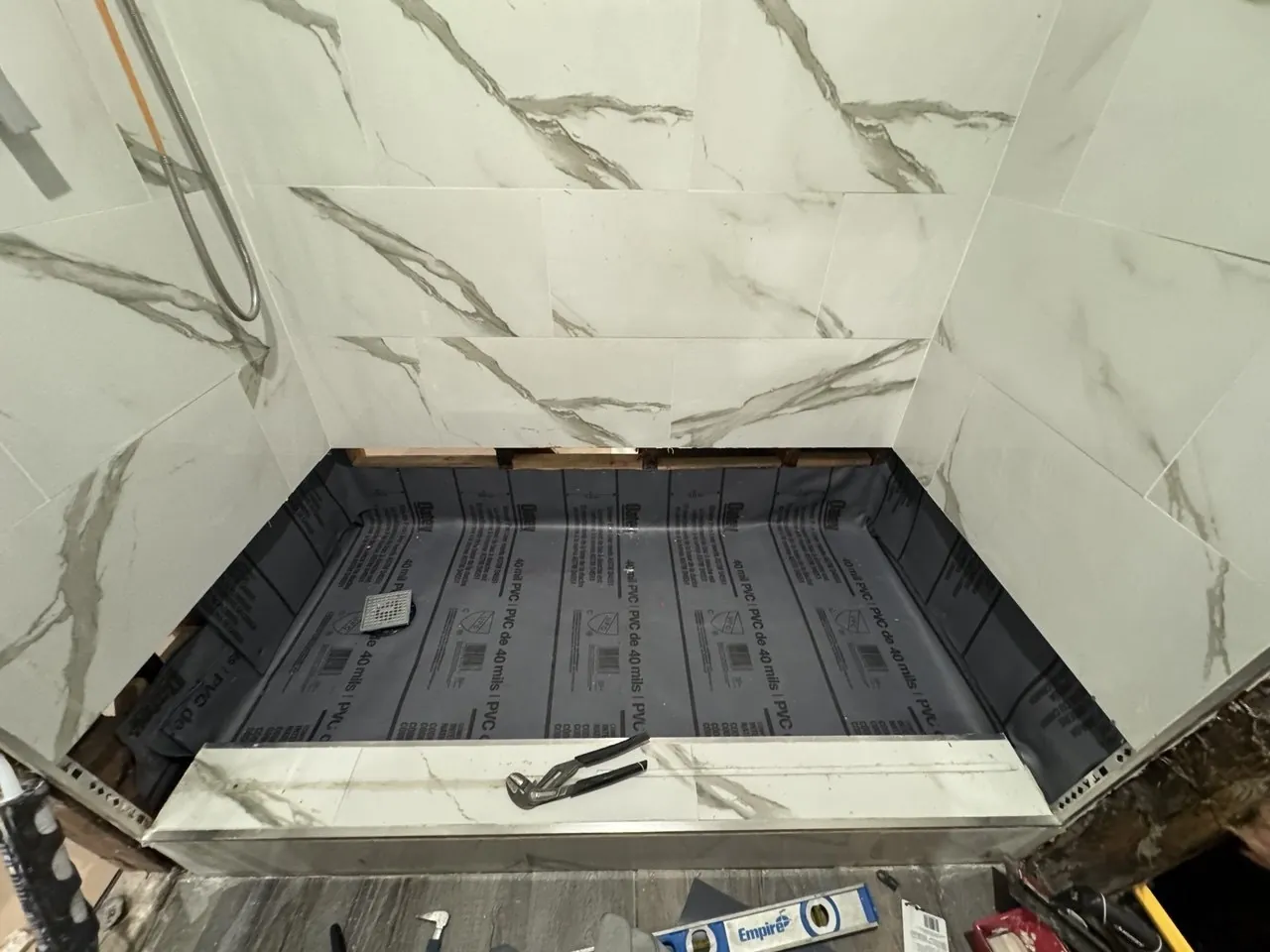 Shower pan lined with PVC waterproofing membrane inside marble-look tiled alcove, before tiling the floor