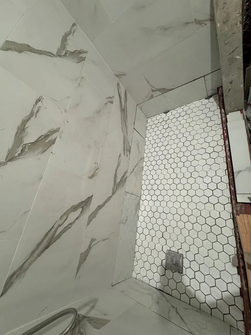 White hexagon mosaic tile floor laid in a new shower with marble-look wall tile