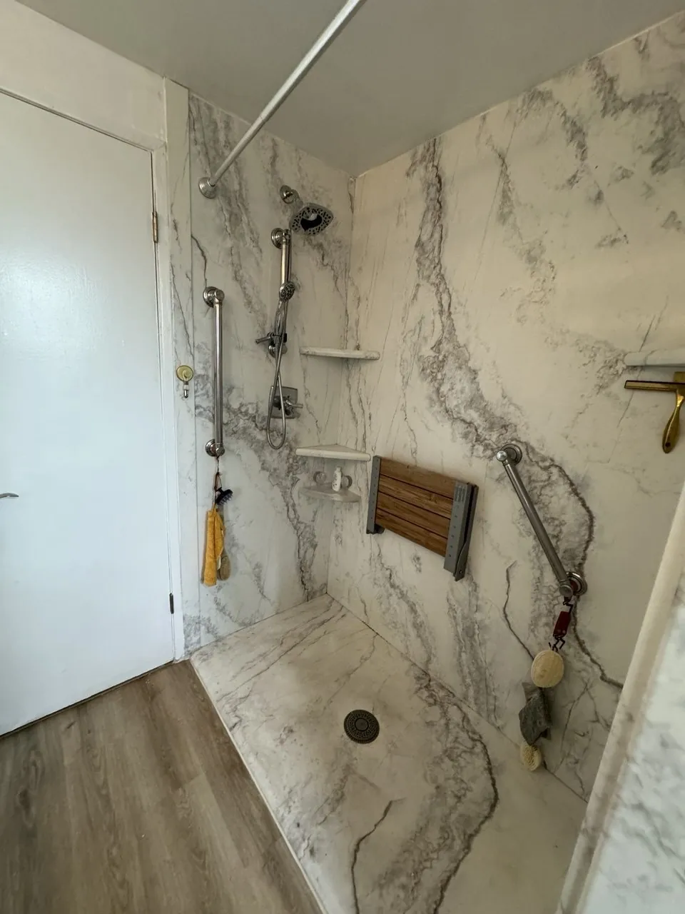 Walk-in shower with full-height marble-look slab walls, folding teak seat and grab bars