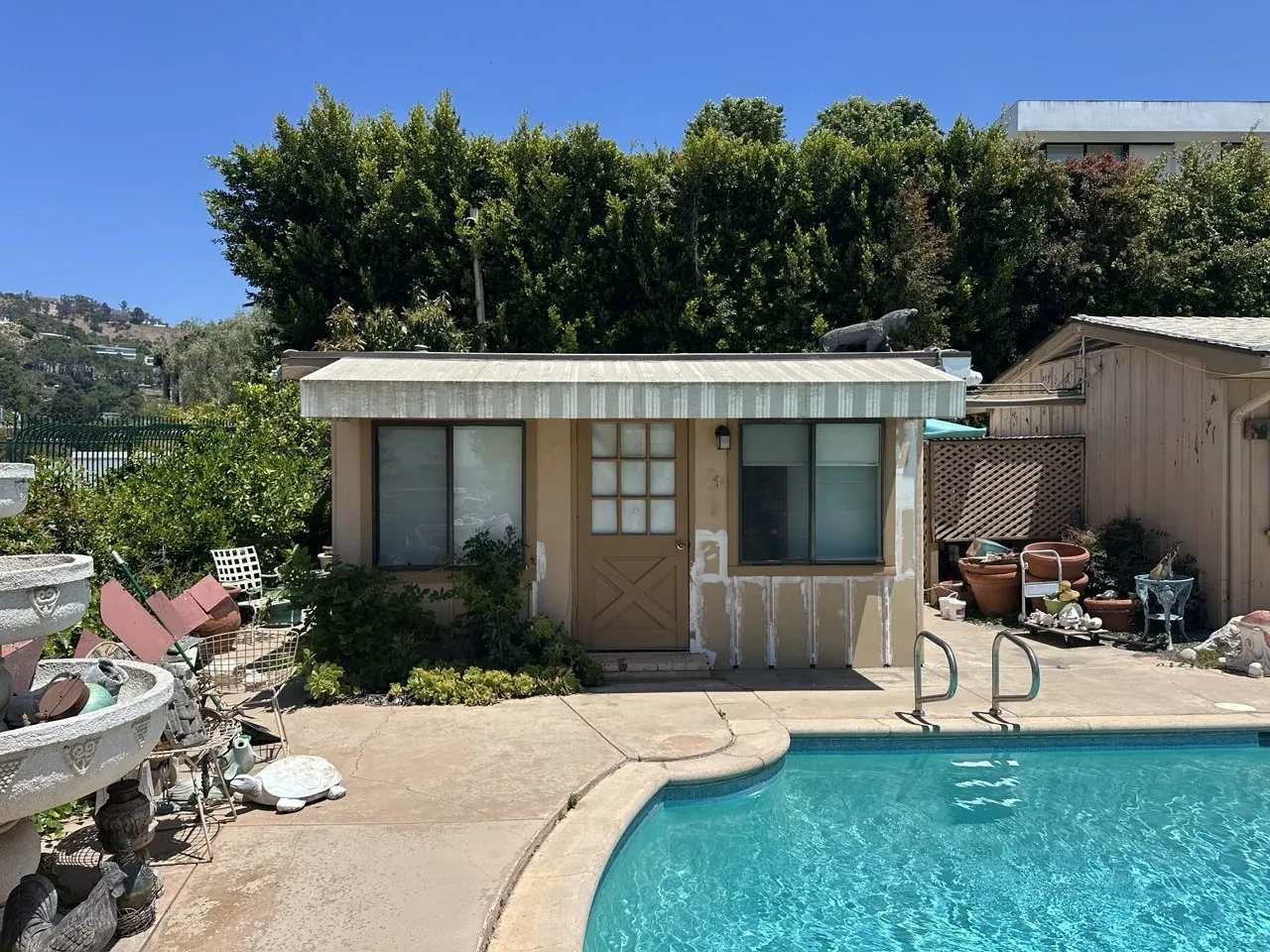 Weathered tan pool house with peeling trim before repainting
