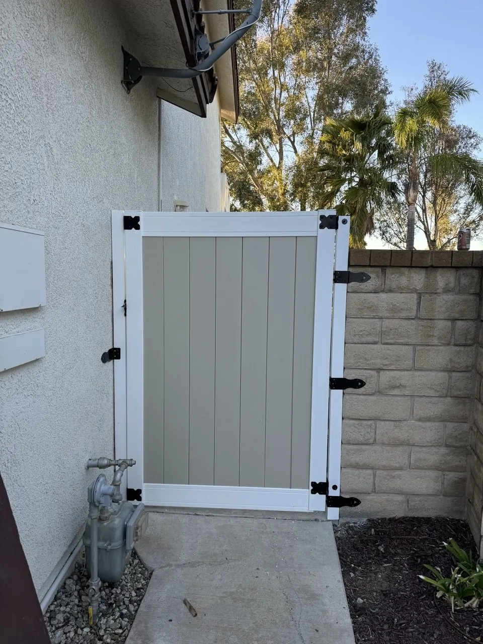 New white and tan vinyl side gate with black hinges between house and block wall